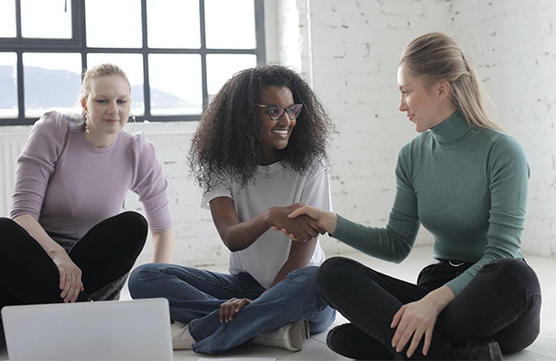 photo of female friends shaking hands while sitting on floor showing support