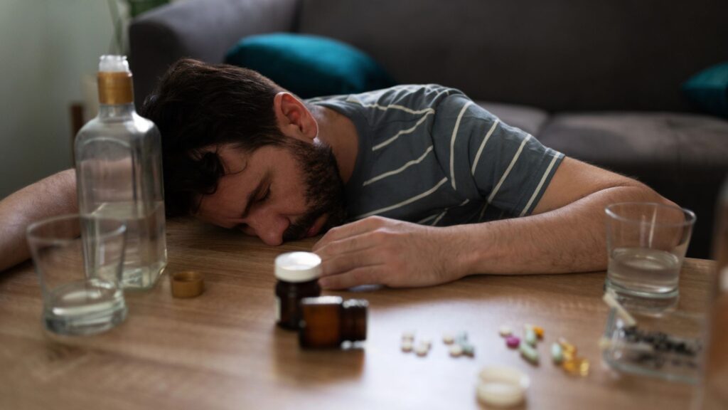 Drunk man passed out on the table surrounded with prescription pills and a bottle of alcohol