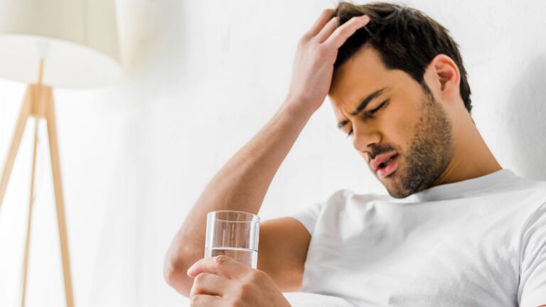 Tired man with headache holding glass of water in bed
