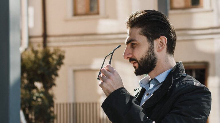 man holding eyeglasses and laptop in a sunny outdoor setting