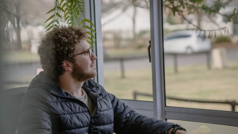 man glasses sits pensively by a window