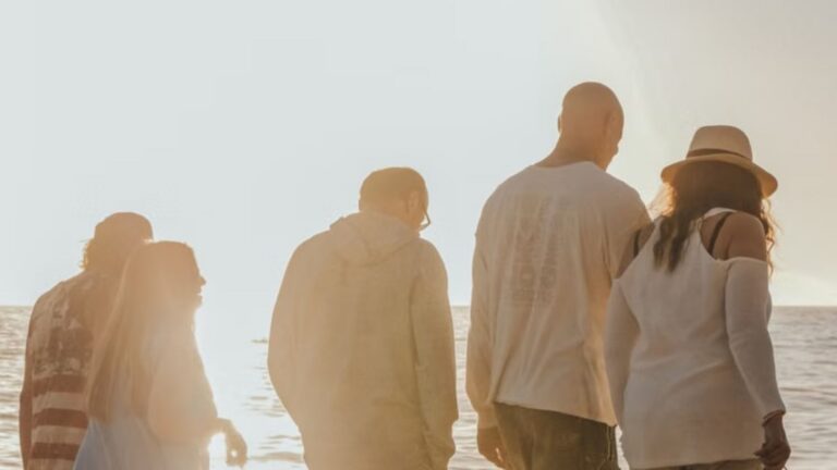 Five friends enjoy a sunny day walking along a sandy beach shore